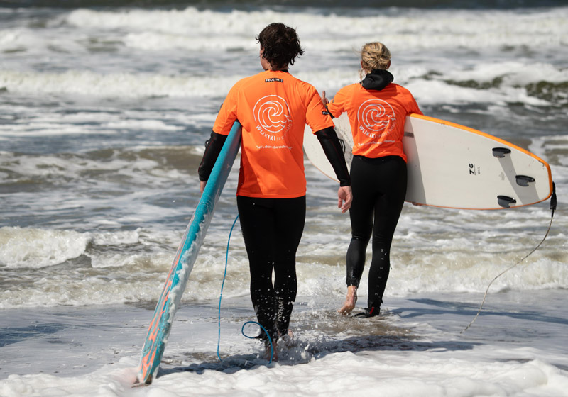 2 personen lopen de zee in met board onder arm